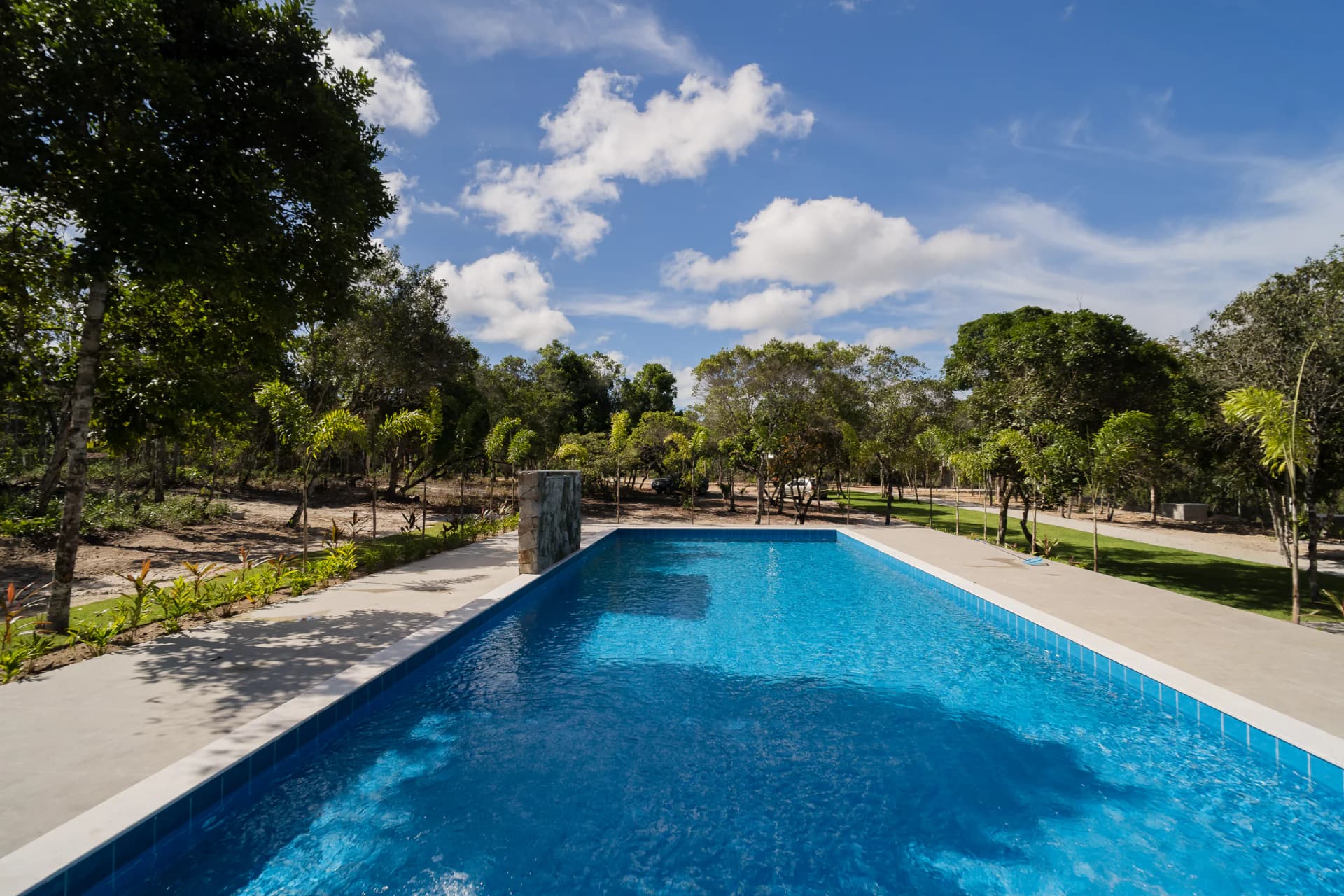 Piscina entre árvores e área de convivência no Residencial Marinho, Arraial d’Ajuda.
