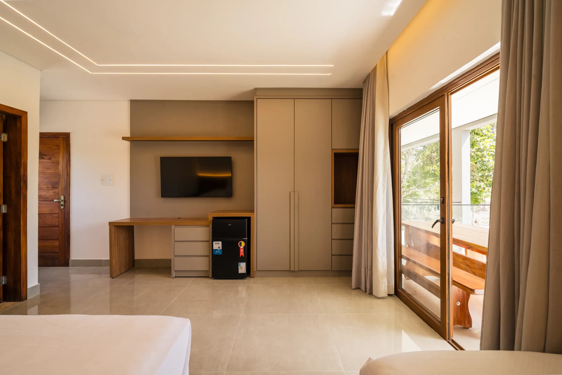 Suíte com televisão e varanda ao fundo no Residencial Marinho, Arraial d’Ajuda.